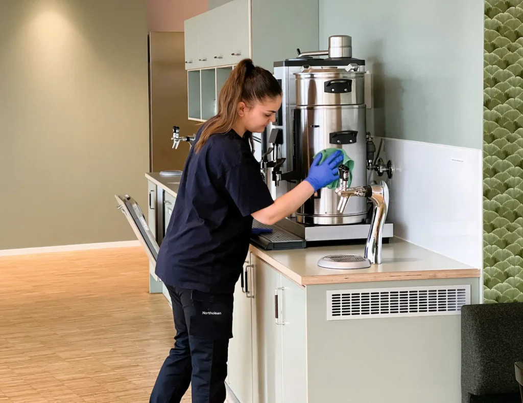 Medarbetare utför storstädning i kontorsmiljö genom rengöring av kök och kaffemaskin